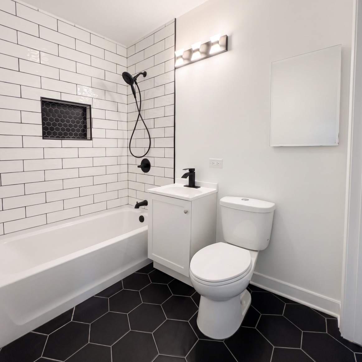 Renovated bathroom with white subway tile and black hexagon floor