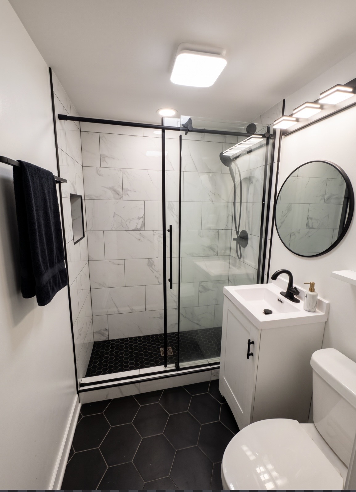 Walk-in glass shower with marble-look tile and black fixtures